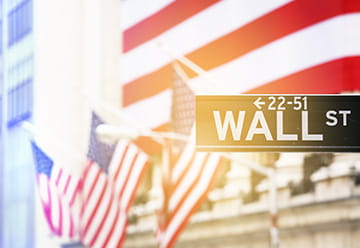 Wall Street street sign with American flags in the background, representing a financial hub and opportunities for immigrants.